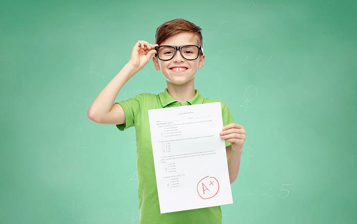 Boy with black plastic rectangular eyeglasses proud to show his A+ report card